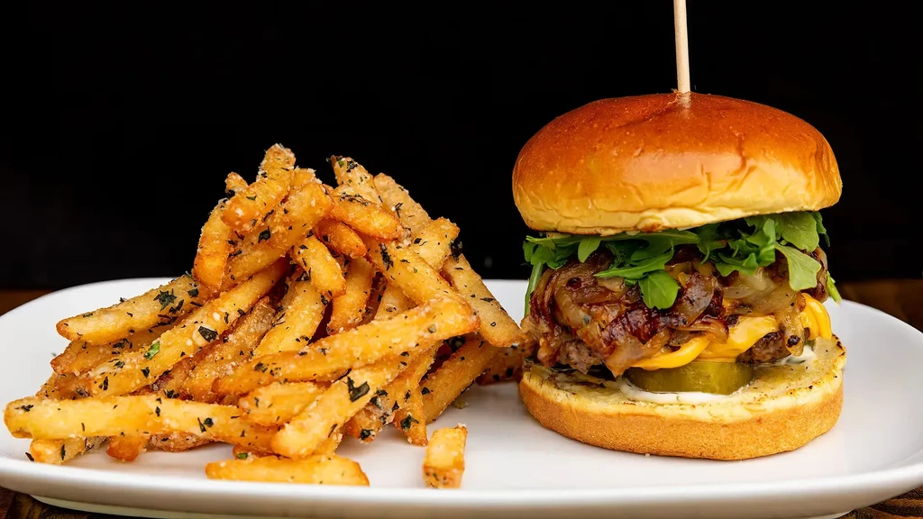 Plated burger with melted cheese, onions, and seasoned fries.