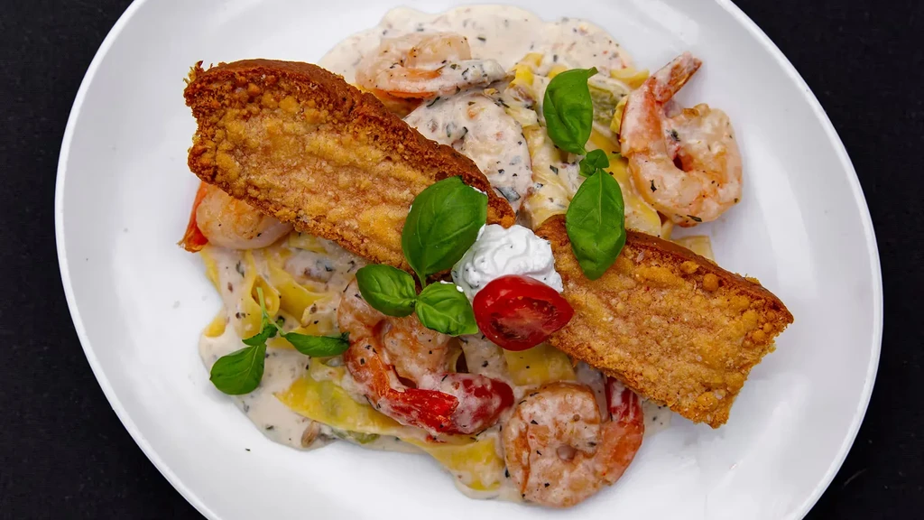 Creamy shrimp pasta garnished with crispy bread, basil, cheese, and tomato.