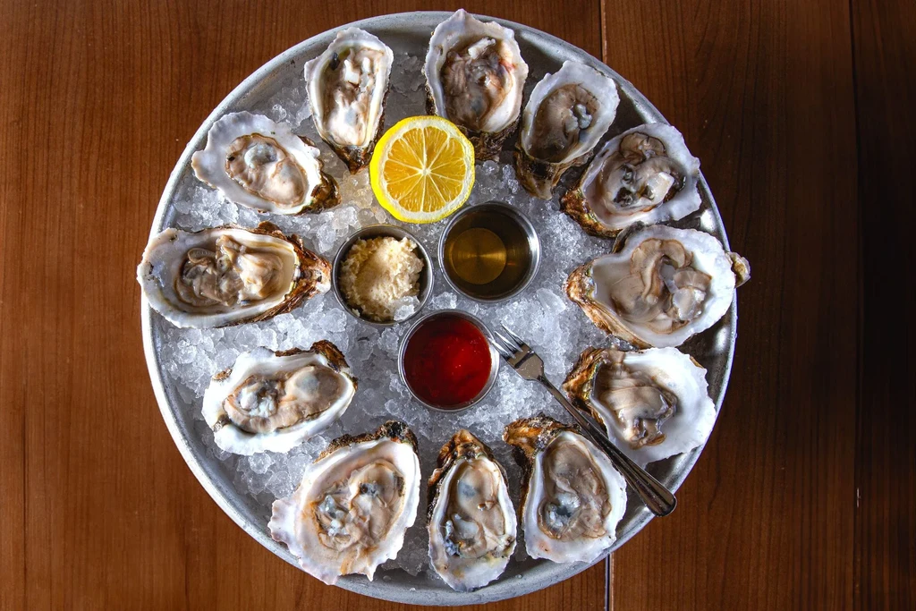 Dozen shucked oysters on ice with lemon and sauces on a platter.