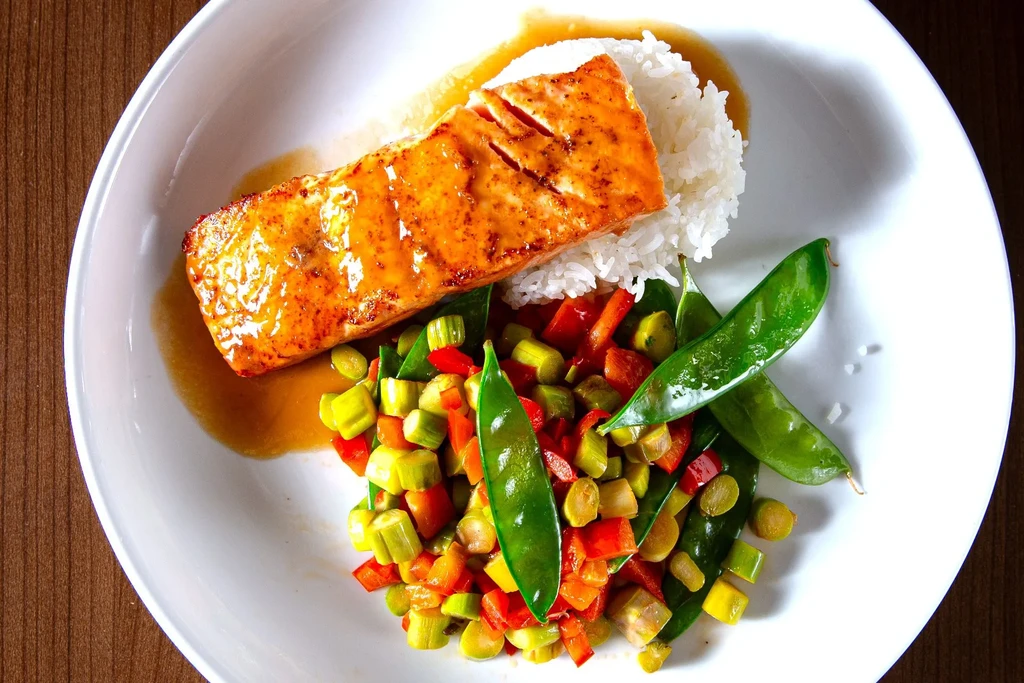 Plated salmon, rice, and colorful vegetables on a white dish.