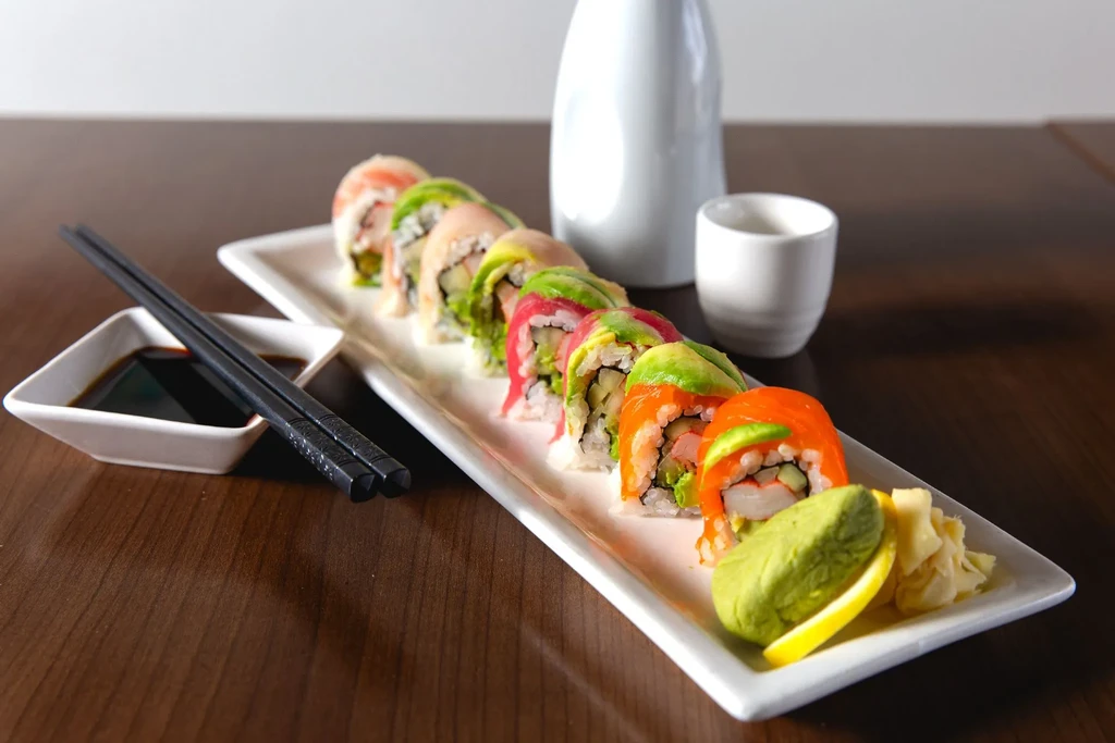 Plate of colorful sushi rolls, wasabi, ginger, soy sauce, and chopsticks.