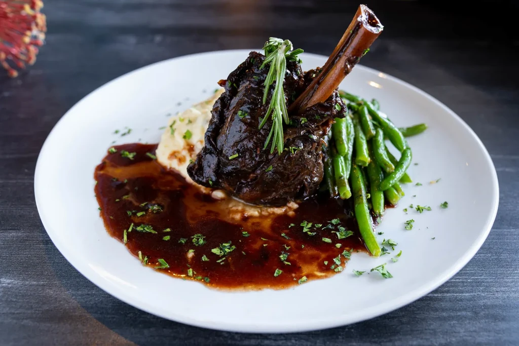 Braised meat with bone, mashed potatoes, green beans, rosemary, and gravy.