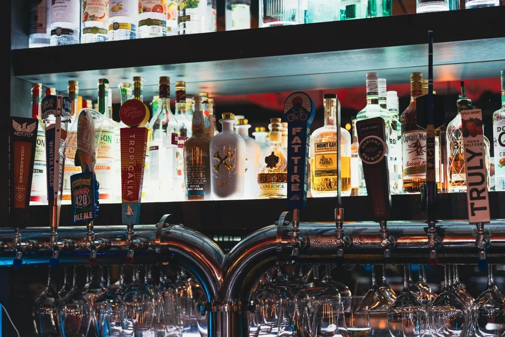 Illuminated bar shelves displaying liquor bottles, diverse beer taps, and glassware.