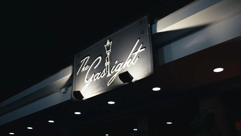 Illuminated 'The Gaslight' sign with a gas lamp logo at night.