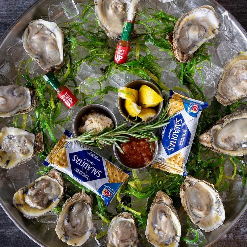 Platter of glistening fresh oysters on ice, with lemon, sauces, crackers.
