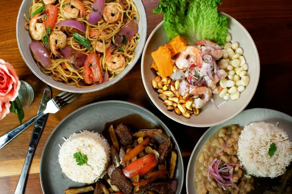 Overhead view of four diverse Peruvian dishes on a wooden table.