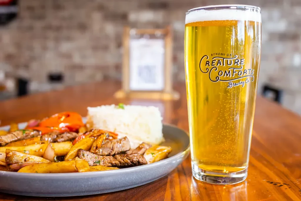 Plate of beef and fries with rice, beside a Creature Comforts beer.