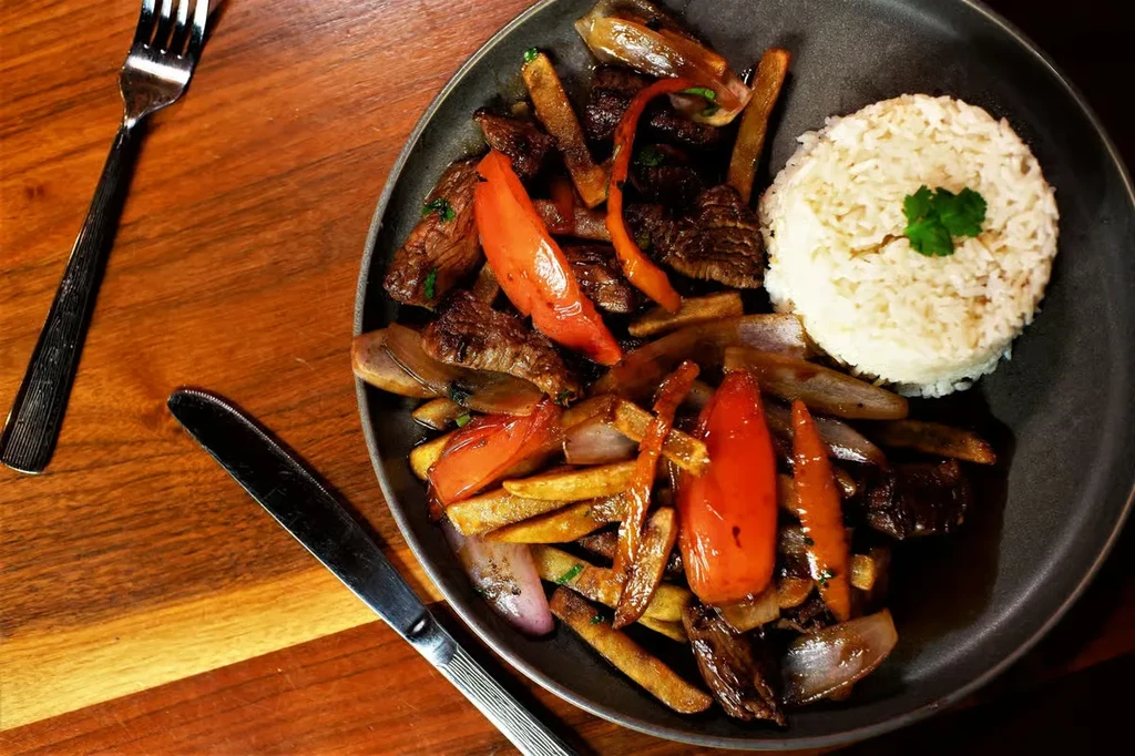 Stir-fried beef, fries, peppers, onions, and rice on a dark plate.