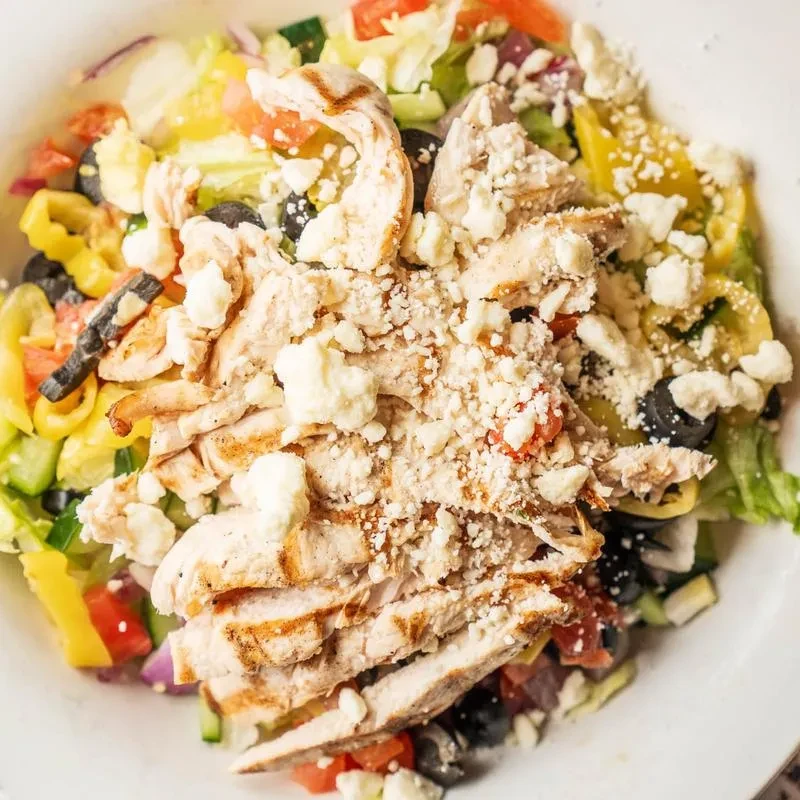 Grilled chicken salad with feta and mixed vegetables in a white bowl.