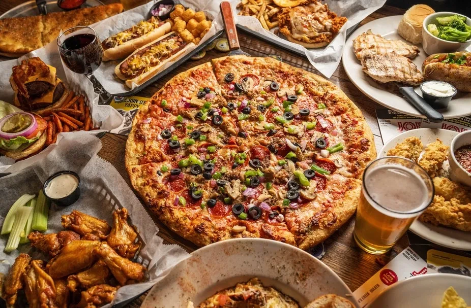 Overhead shot of pizza, wings, burgers, and drinks on a table.