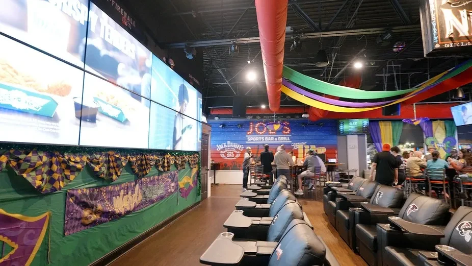 Joe's Sports Bar interior, Mardi Gras decor, Falcons recliners, large video wall.
