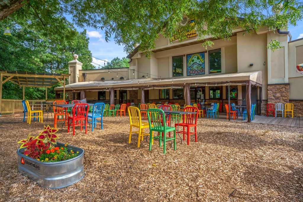 Sunny outdoor restaurant patio with colorful chairs, wood chips, and murals.