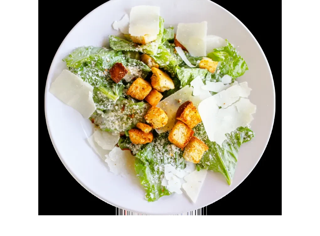 Overhead shot of Caesar salad with romaine, croutons, Parmesan, and seasoning.