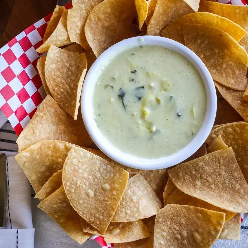 Bowl of creamy green dip surrounded by tortilla chips.