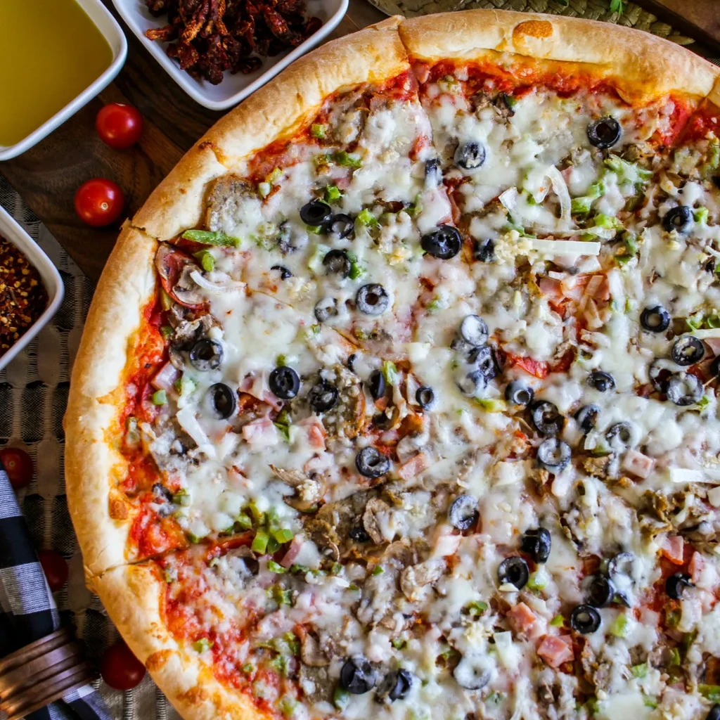 Freshly baked pizza with cheese, olives, peppers, mushrooms, and ham.