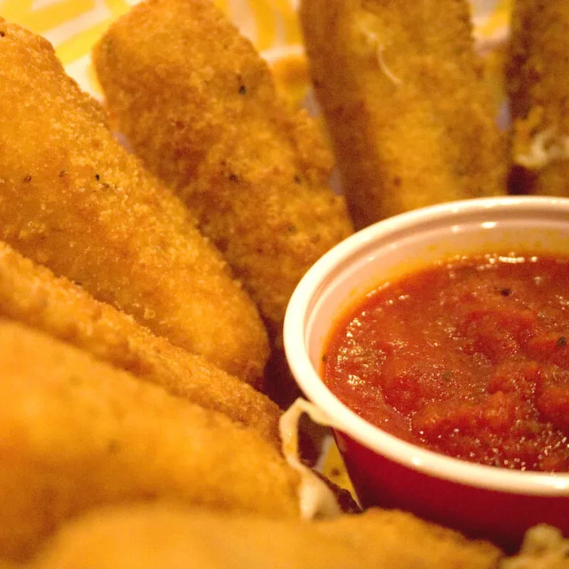 Basket of fried mozzarella sticks with melted cheese and marinara sauce.