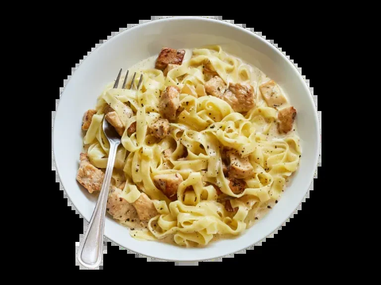 White bowl of creamy chicken fettuccine with black pepper and a fork.