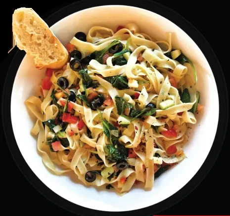 Overhead view of fettuccine pasta with tomatoes, olives, greens, and bread.