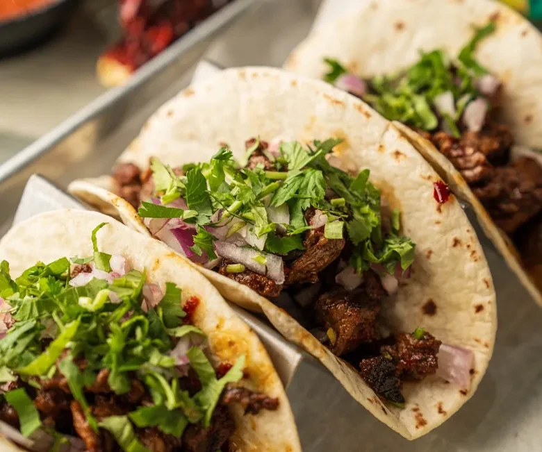 Three char-marked tacos with meat, cilantro, and red onions.