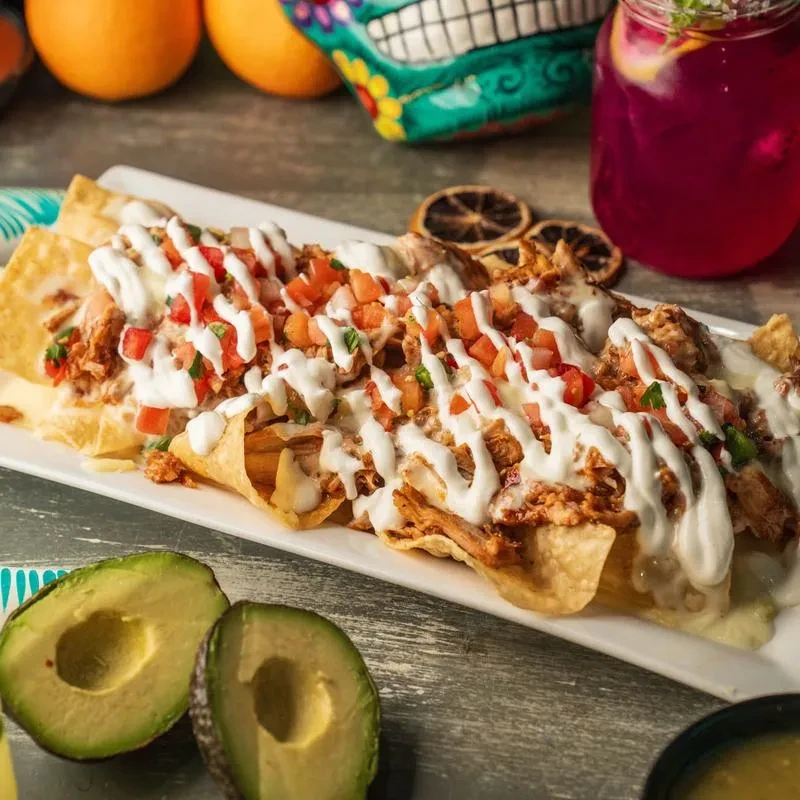 High-angle shot of loaded chicken nachos with pico de gallo and avocado.