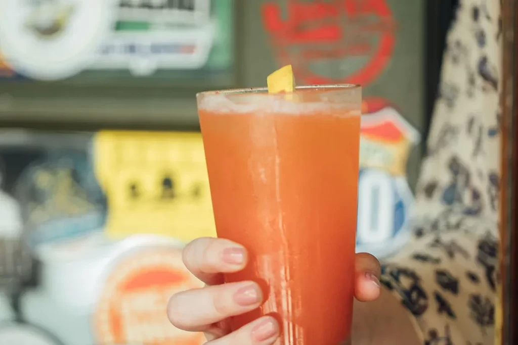 Close-up of a hand holding an orange drink with a citrus wedge.