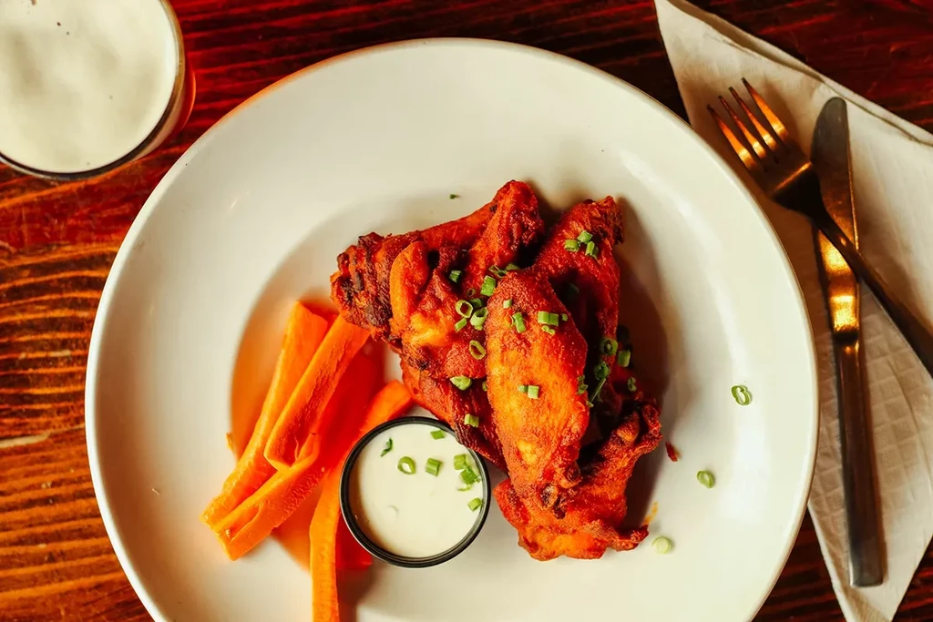 Crispy chicken wings, green onions, dipping sauce, and carrots on wood.