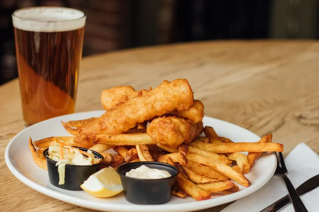 Classic fish and chips with coleslaw, sauce, lemon, and beer.