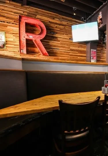 Empty restaurant booth, wooden wall, red neon 'R' and blank TV.