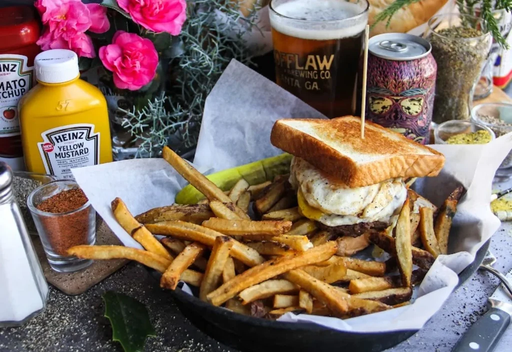 Egg sandwich, fries, pickle, and beer in cast iron pan.