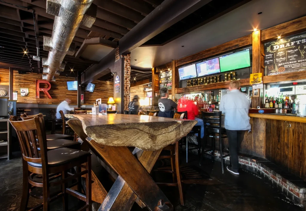 Bar interior: live-edge table, long bar with taps, and patrons.