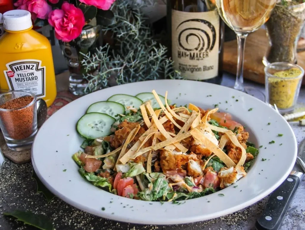 Close-up of a fried chicken salad with vegetables, tortilla strips, and wine.