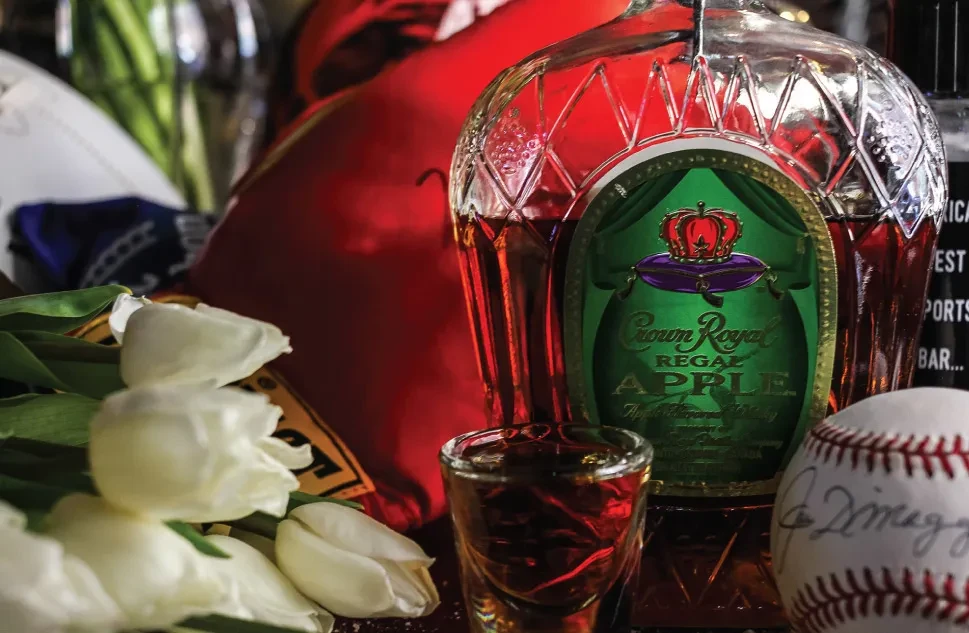 Crown Royal apple whiskey bottle, shot glass, tulips, and signed baseball.