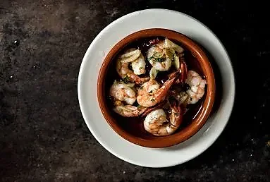 Garlic shrimp served in a clay cazuela on dark table