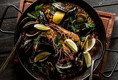 Seafood paella pan with mussels, clams, prawns and lemon wedges