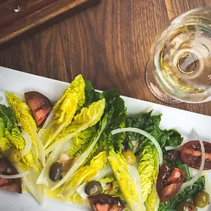 Little gem salad with olives and tomatoes beside white wine