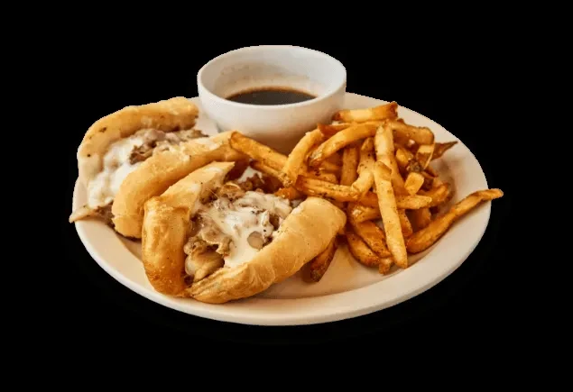 Two cheesesteak halves, french fries, and dipping sauce on a white plate.
