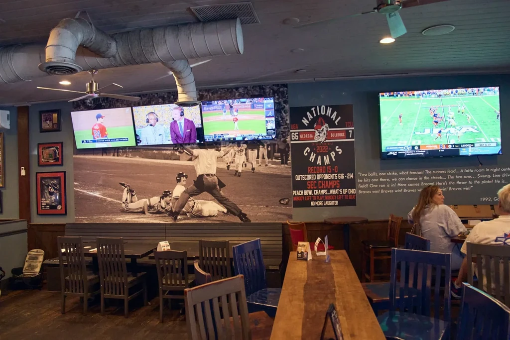 Sports bar interior with TVs displaying games, memorabilia, and a baseball mural.