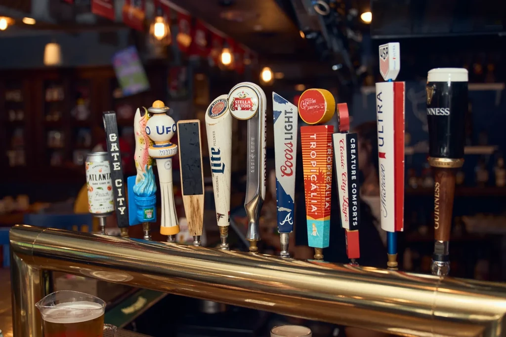 Diverse beer taps and a glass of amber beer on a bar.