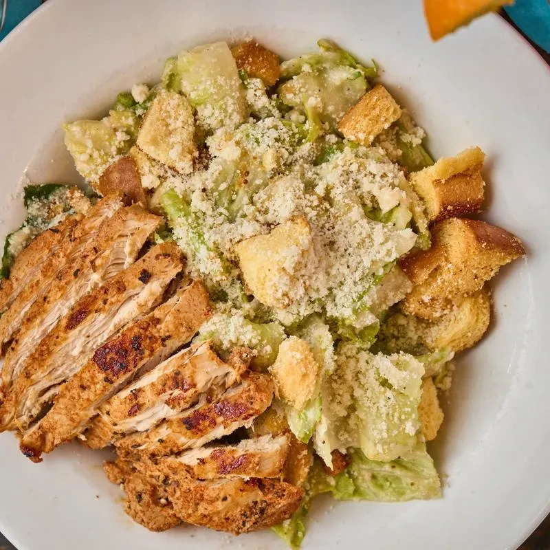 Close-up Caesar salad with grilled chicken, croutons, Parmesan, white bowl.