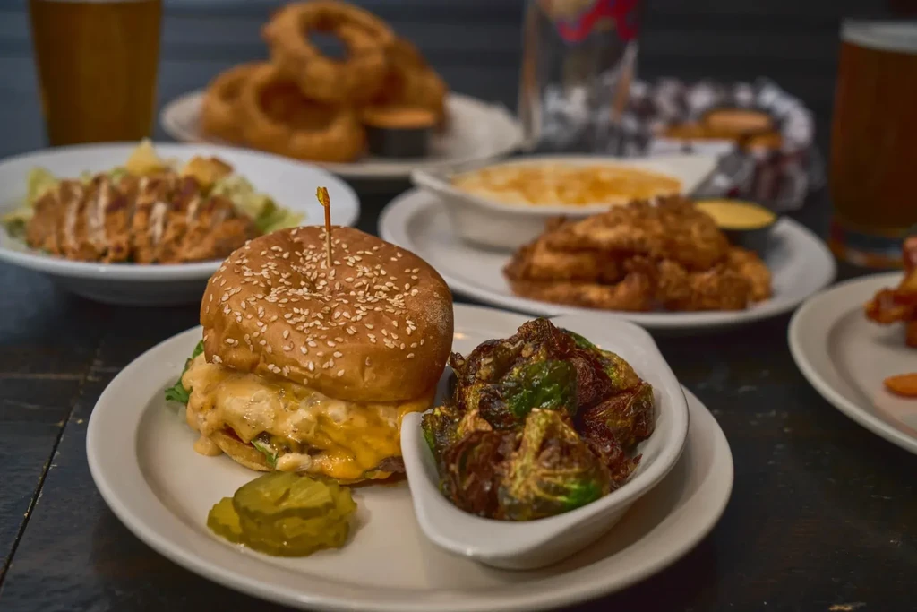 Close-up of a cheeseburger, Brussels sprouts, and other comfort food on a table.