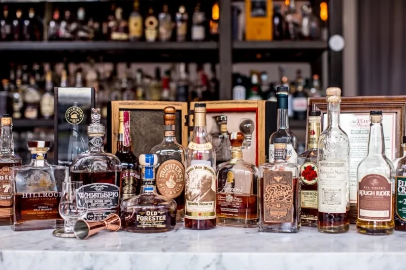 Collection of whiskey and bourbon bottles on marble with tasting glass.