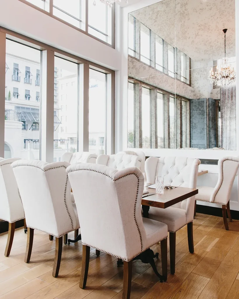 Bright, elegant restaurant interior with cream chairs, city views, and chandelier.