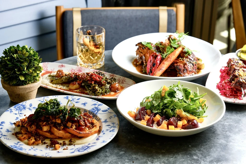 Gourmet spread of five dishes and a drink on a dark table.