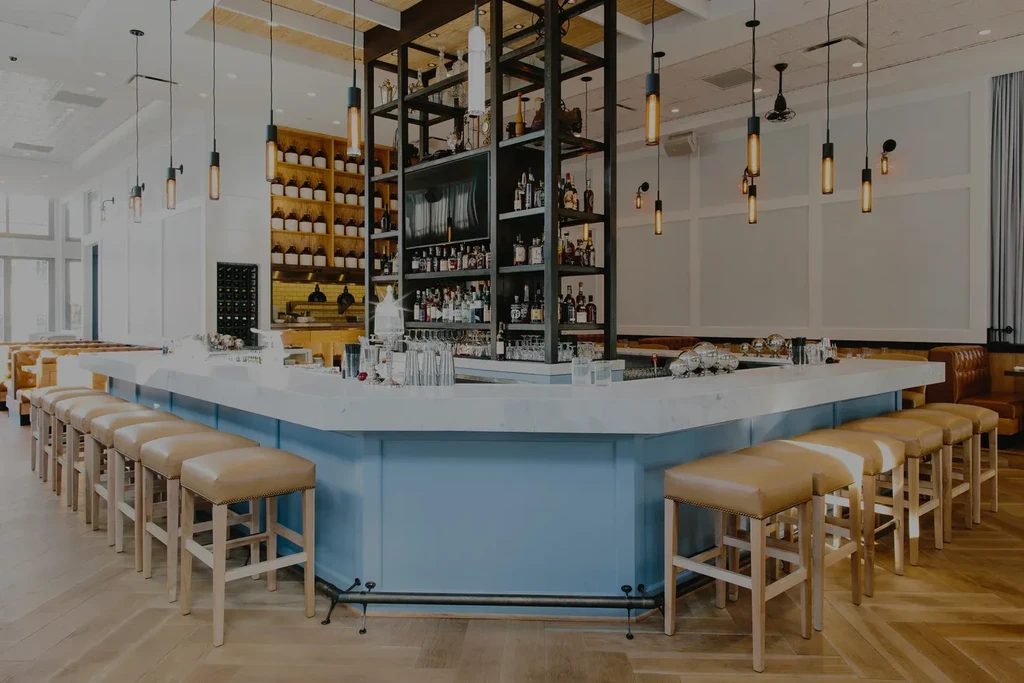 Modern bar with L-shaped marble counter, blue base, and liquor bottles.