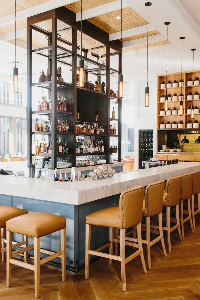 Modern bar with liquor display, marble counter, tan stools, and wood floor.