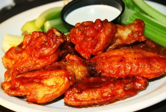 Close-up of a plate of buffalo wings, celery, and dipping sauce.