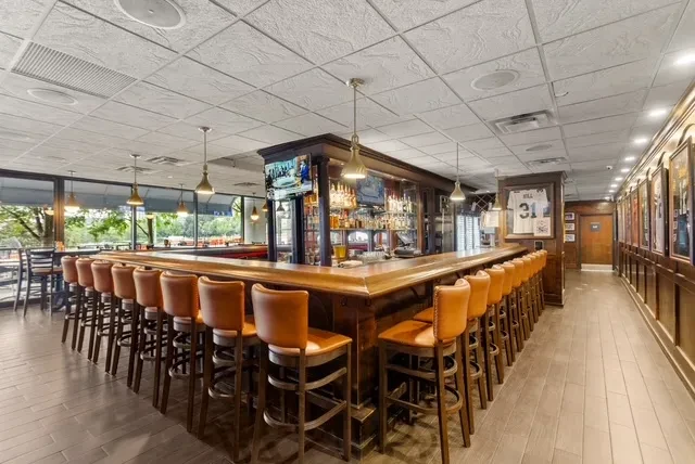 L-shaped wooden bar with liquor display, TVs, and sports memorabilia.