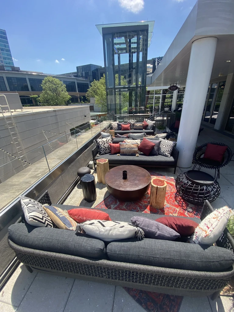 Sunny patio with grey sofas, patterned pillows, rug, and city view.