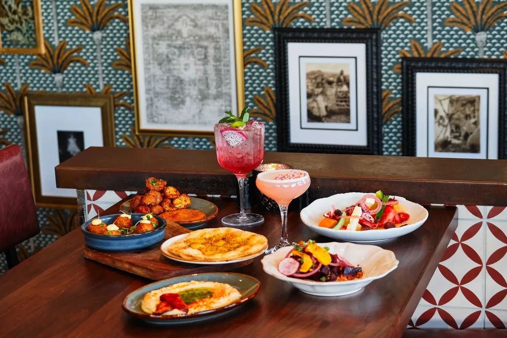Colorful food dishes and two cocktails on a dark restaurant table.
