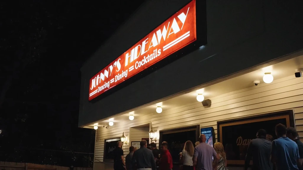 Johnny's Hideaway at night, bright red sign, people at entrance.